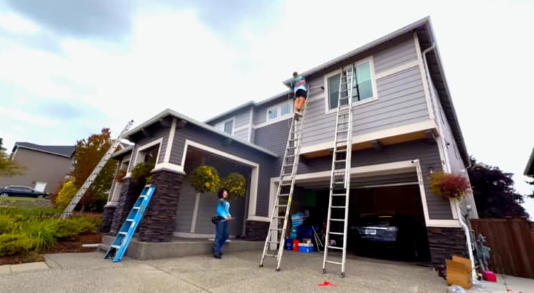 Crew on ladders installing permanent lighting track along the roofline of a two-story home
